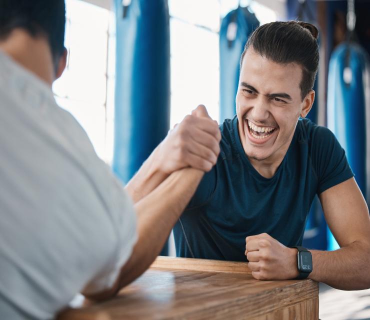 Strong, active and men arm wrestling in the gym on a table while being playful for a challenge. Riv.